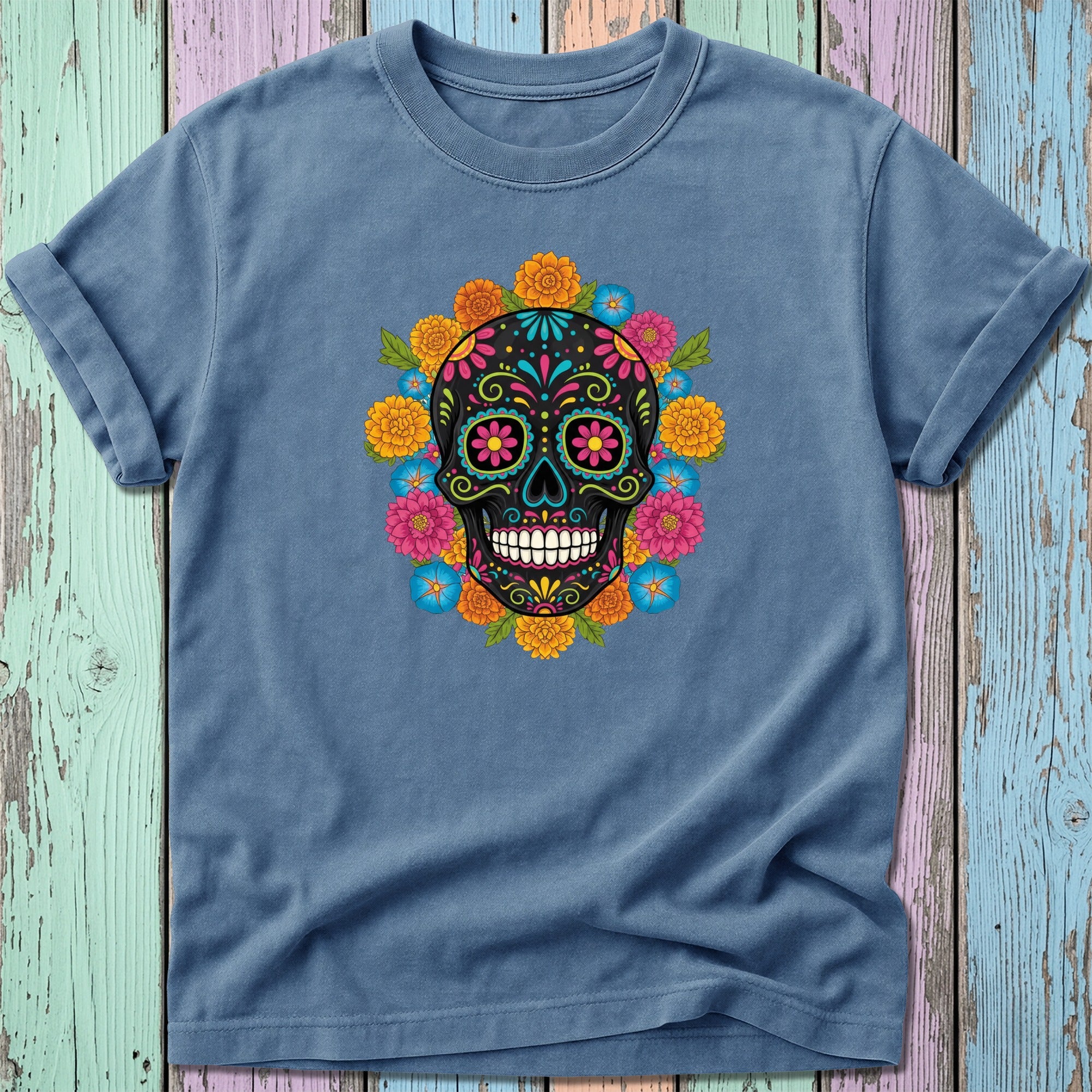 Blue t-shirt with colorful sugar skull and floral design on a distressed wooden background.