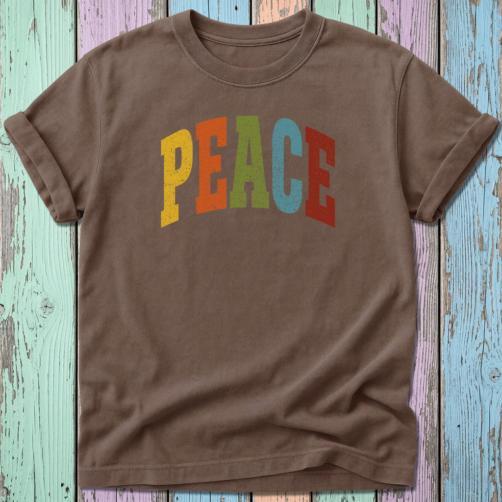Brown t-shirt with colorful "PEACE" text on a distressed wood background.
