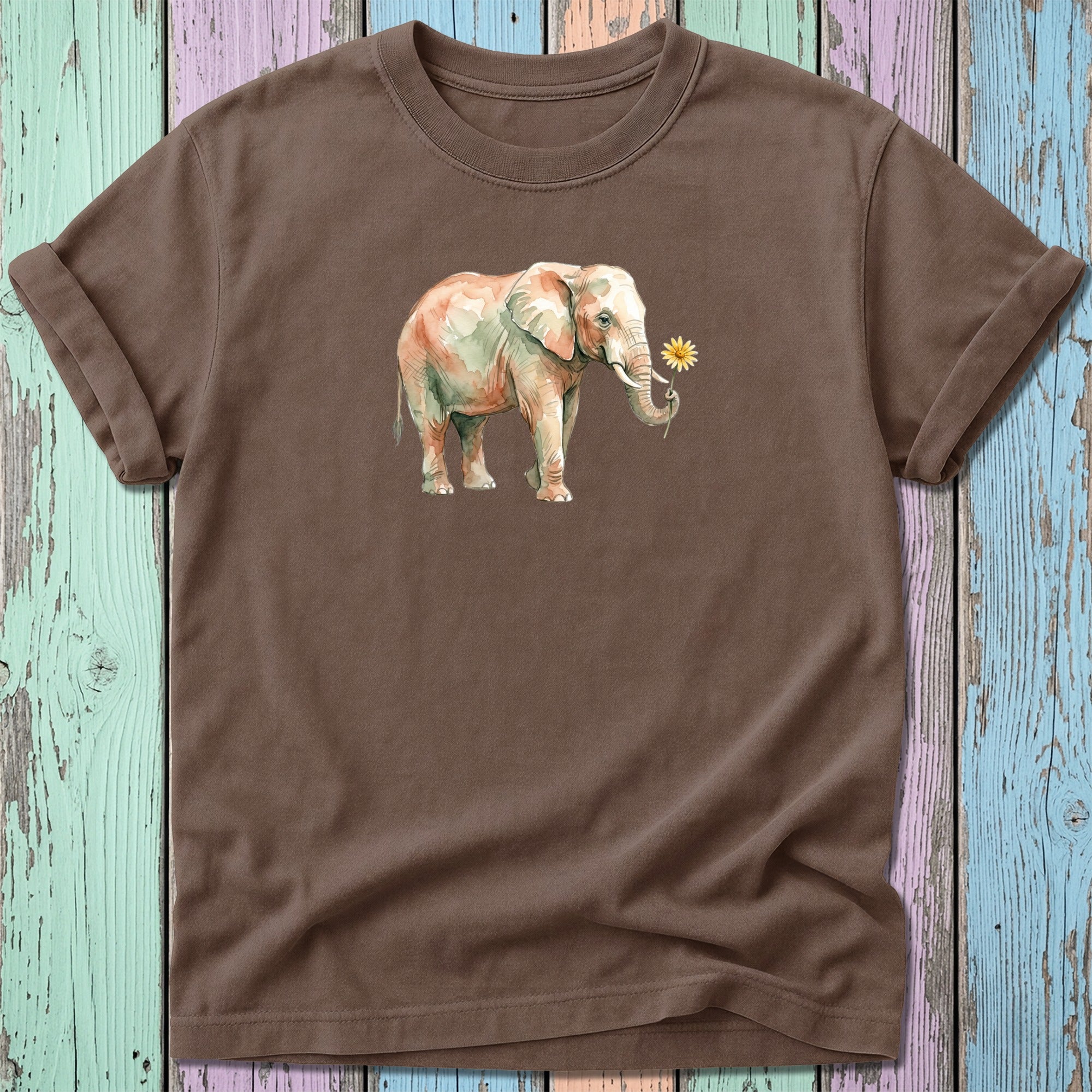 Watercolor elephant with flower on brown t-shirt, against colorful wood background.