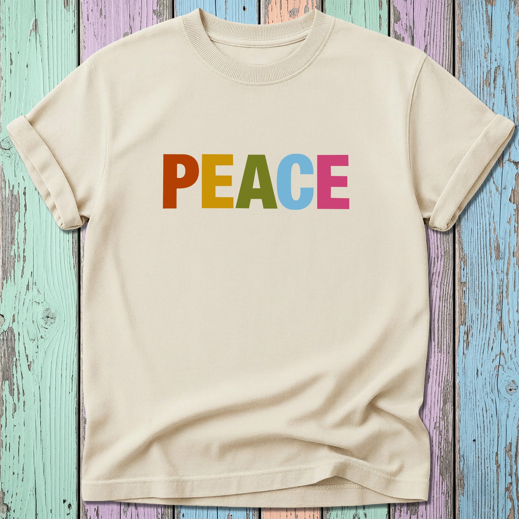 Cream t-shirt with colorful "PEACE" text on a distressed wooden background.