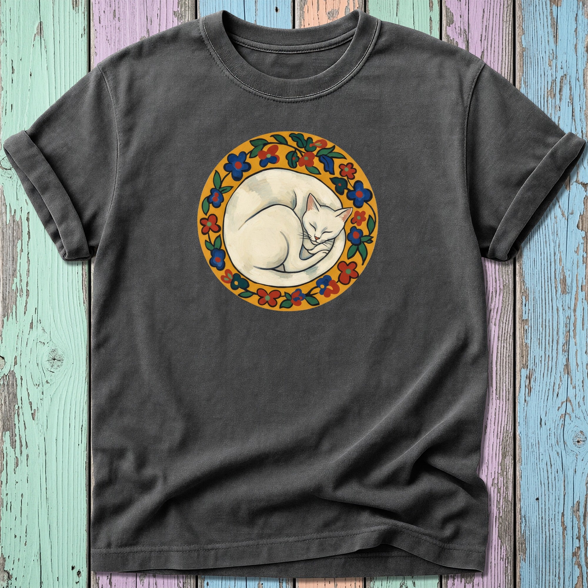 Cream-colored cat curled asleep within a floral circular frame on a dark t-shirt.