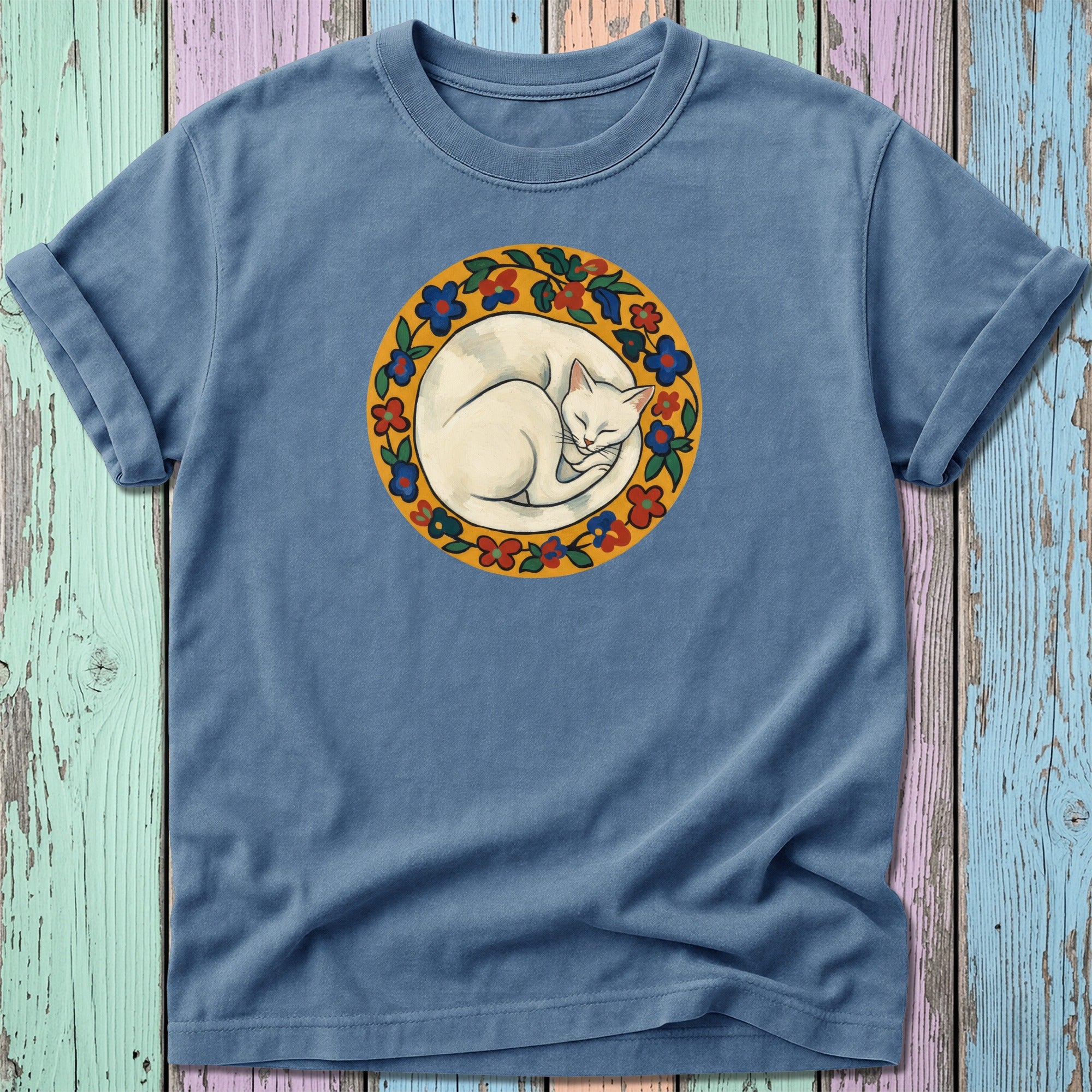 White cat sleeping curled up in a floral medallion on a blue t-shirt.
