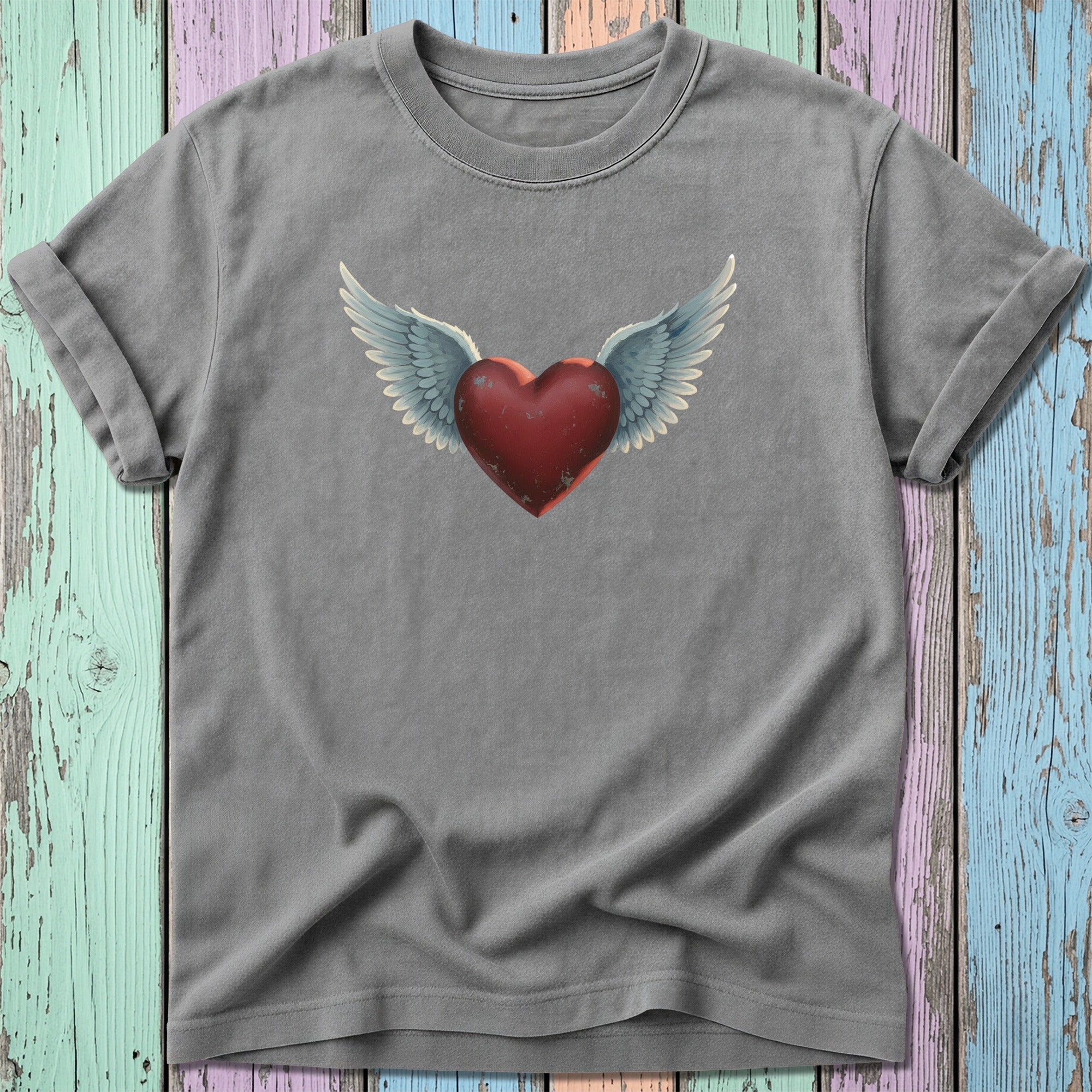 T-shirt with a winged heart graphic on a distressed, multicolored background.